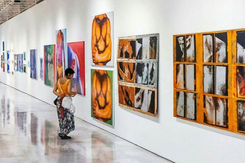 Art gallery with a visitor looking at artwork on a white wall.